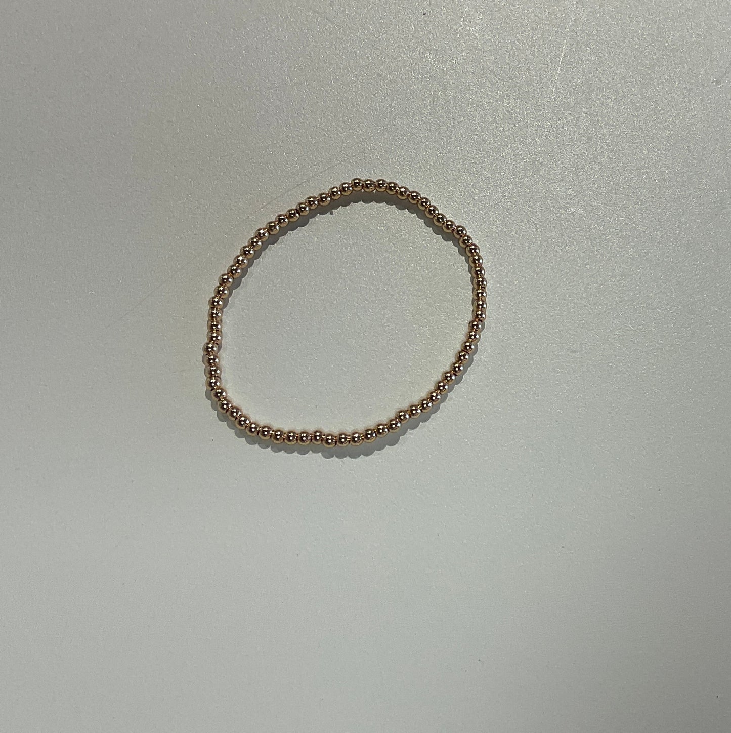 A thin beaded stretch bracelet in a warm gold tone, displayed on a plain white surface.
