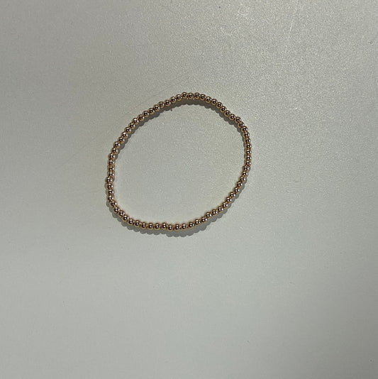 A thin beaded stretch bracelet in a warm gold tone, displayed on a plain white surface.